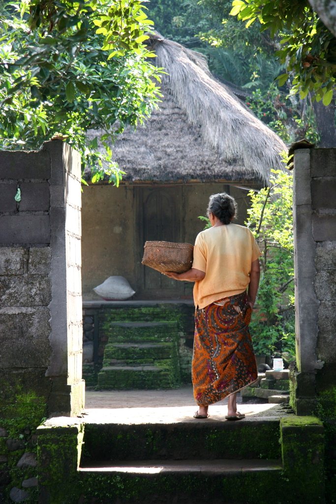 Woman carrying a basket through a traditional village compound gateway — cultural access on a bespoke Asia journey